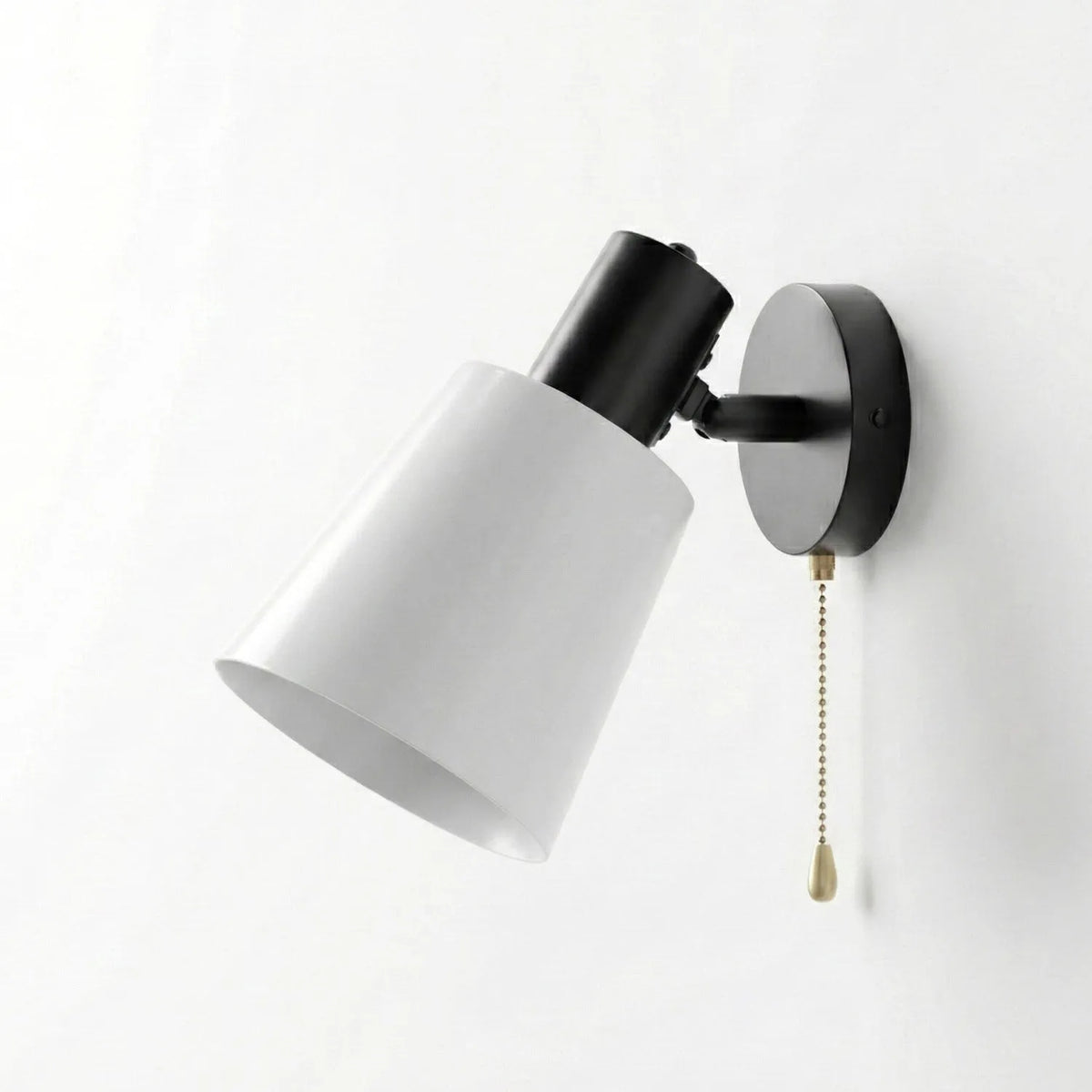 modern adjustable wall sconce featuring a matte black base, a pivoting joint, a white conical shade, and a gold pull-chain switch