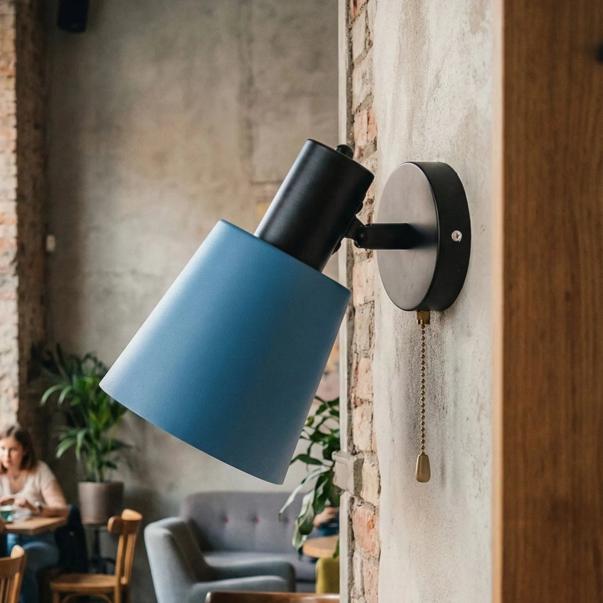 A cone-shaped metal shade in blue paired with a matte black wall mount and arm.