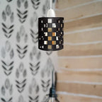 A black metal pendant light with a cylindrical cage design and square cutouts