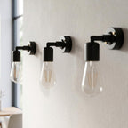 Three black industrial wall sconces with clear glass Edison bulbs mounted 