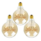G125 E27 LED filament bulb with Love script filament, amber glass, lit, three bulbs on a white background
