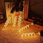 T185 E27 LED filament bulb, amber glass, spiral filament, lit, four bulbs on a fabric surface