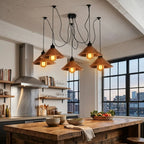 Five copper cone pendant lights with black cords and warm glowing bulbs, hanging over a rustic wooden kitchen island in a modern loft kitchen.