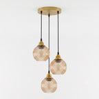 Three-light pendant ceiling fixture with ribbed amber-tinted glass shades and brass-toned metal hardware, suspended from a round ceiling canopy against a plain white wall.