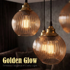 Two hanging pendant lights with ribbed clear glass shades and warm brass-toned tops, shown in a dimly lit interior. Text at the bottom reads 'Golden Glow' and 'Timeless Elegance in Every Light.