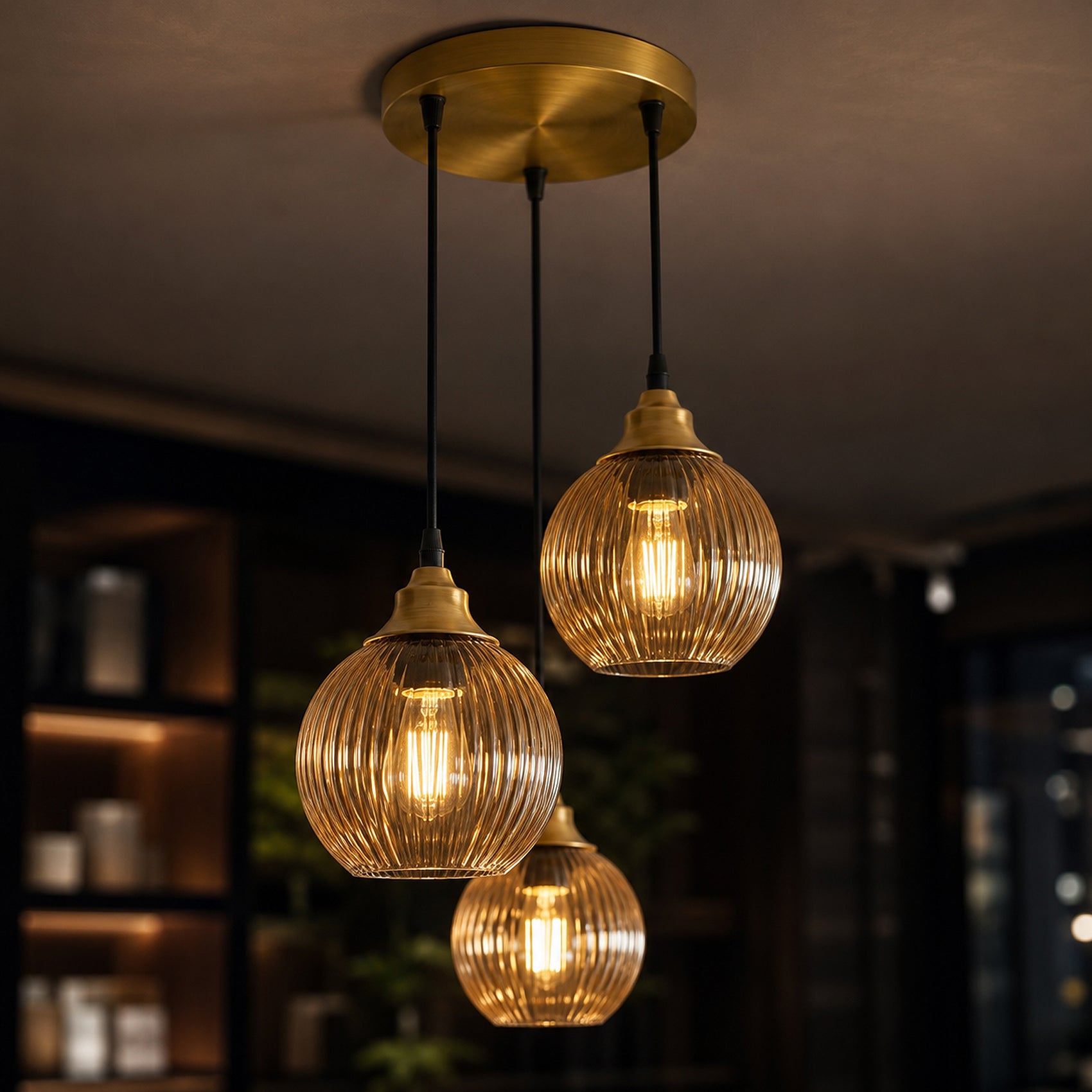 Three hanging pendant lights with ribbed clear glass shades and warm brass-toned caps, suspended from a round ceiling canopy in a dimly lit interior.