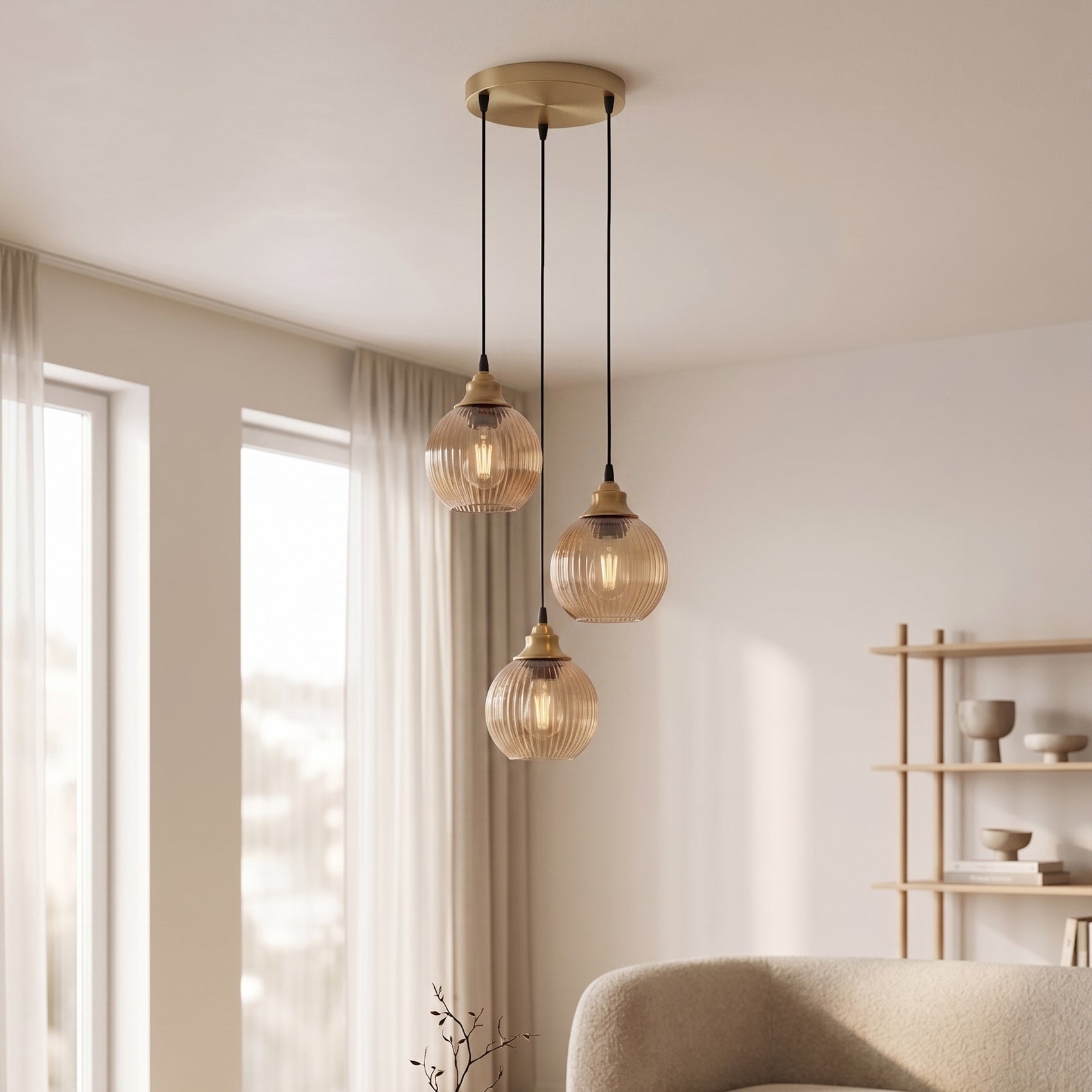 A modern three-light pendant ceiling fixture with ribbed amber-tinted glass shades and a brushed brass finish, hanging in a bright, contemporary living room.