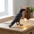 Black bird-shaped lamp with a light bulb on a wooden surface