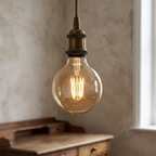 Vintage-style light bulb hanging in a room with a wooden desk and window.