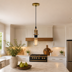 A brass and black pendant light hangs over a kitchen island with a marble countertop.