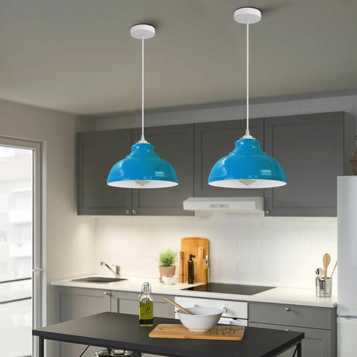 Two blue metal lamp shades with white interiors, suspended by white cords in a kitchen, unlit.