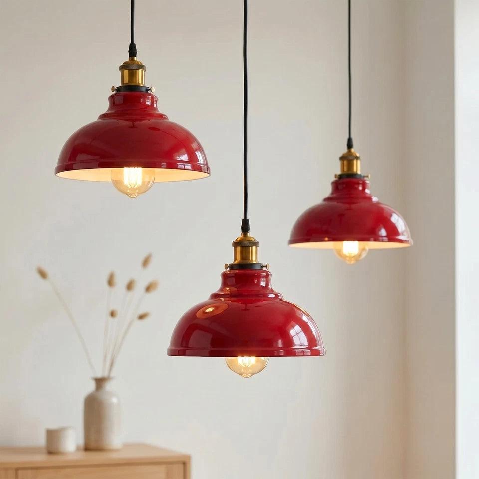 Three red metal lampshades with brass fittings, suspended by black cords in a living room setting, lit.