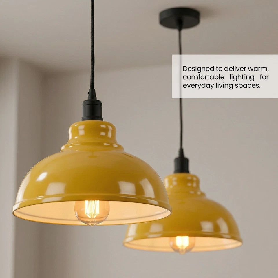 Two modern pendant light fixtures with glossy mustard yellow dome shades and black cords, shown hanging in a minimalist interior setting. A text overlay on the right reads, 'Designed to deliver warm, comfortable lighting for everyday living spaces.