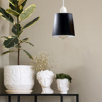 A black metal lamp shade hangs lit above a shelf with decorative planters and a potted plant.