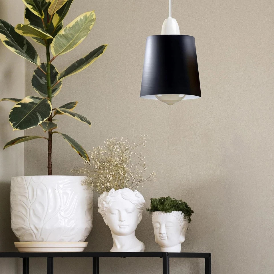 A black metal lamp shade hangs lit above a shelf with decorative planters and a potted plant.