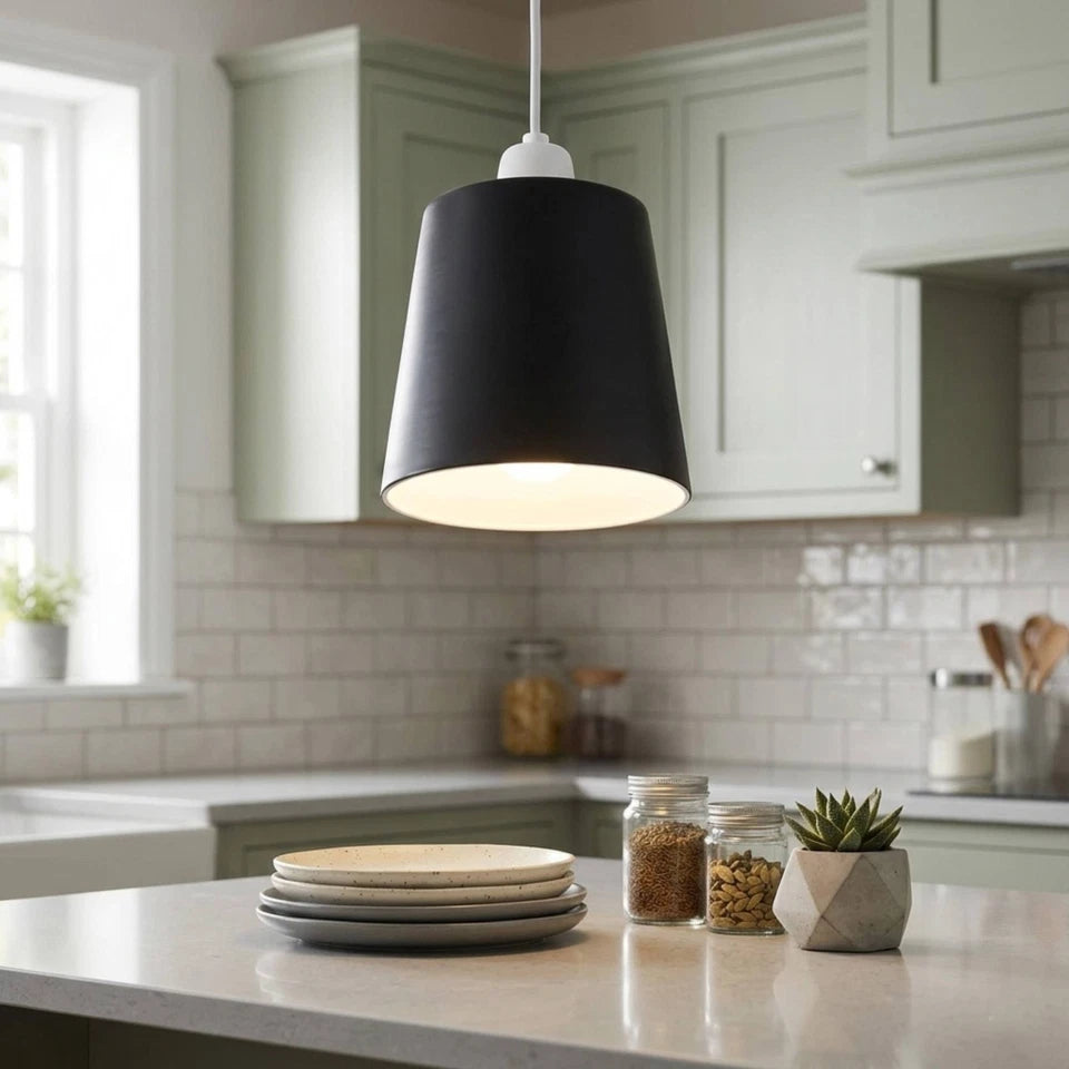 A black metal lamp shade hangs lit in a kitchen with white cabinets and a tiled backsplash.