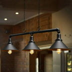 A steampunk ceiling light with three lit bulbs in black shades, hanging over a dining area with brick walls.