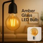 An amber glass LED light bulb with a visible filament, shown illuminated on a black lamp fixture against a warm indoor background.